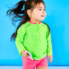 Toddler girl walking playfully wearing neon green rash guard and neon pink euro swim shorts while holding a pair of white sunglasses