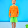 Child smiling and wearing children's neon orange rash guard with a neon green collar and neon green swim trunks.