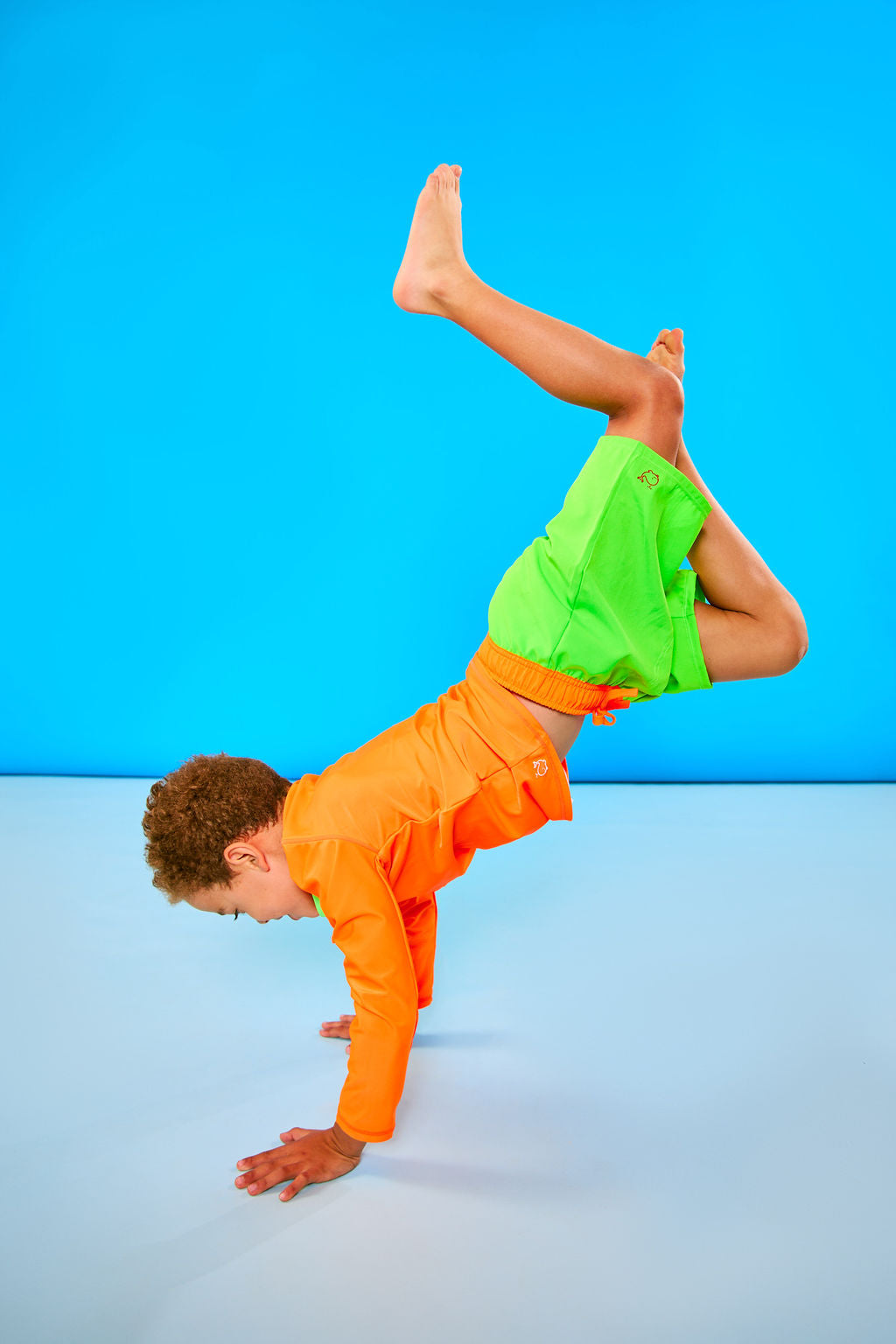 Child doing headstand while wearing neon green swim trunks with a neon orange waistband.