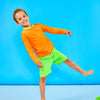 Child smiling and standing playfully while wearing children's neon orange rash guard with a neon green collar